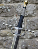 European hand and a half longsword with a brass pommel and intricate grip against a stone wall.
