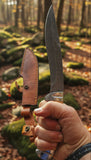 Replica Persian Fighting Knife with Damascus Blade Man At Arms held in hand with leather sheath in outdoor setting.