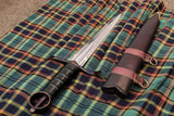 A Kern Irish Companion Dagger with a carbon steel blade, black grip, and a wooden scabbard with leather fittings, displayed on a plaid background.