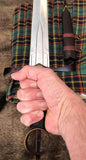 Irish Kern companion dagger held in hand with plaid fabric background.