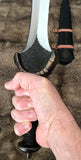Celtic leaf blade war sword with hand gripping the hilt and scabbard in the background, showcasing craftsmanship.