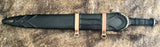 Celtic leaf blade war sword in a black leather sheath with decorative elements and leather straps.