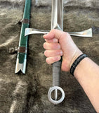 Irish hand and a half sword by Kingdom Of Arms held in hand with scabbard in background.