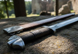 The Saxon Langsax or Long Seax lying on a stone surface next to a leather sheath, showcasing its craftsmanship.
